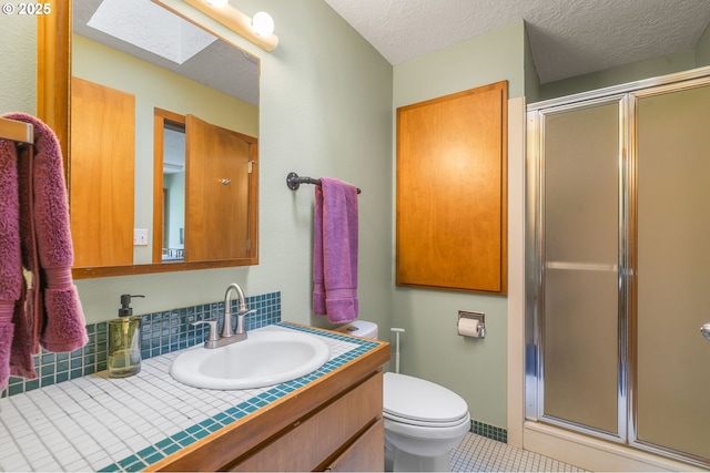 full bath featuring toilet, a stall shower, a textured ceiling, a skylight, and vanity