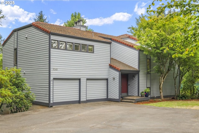 view of front of home with a tile roof, an attached garage, driveway, and a chimney