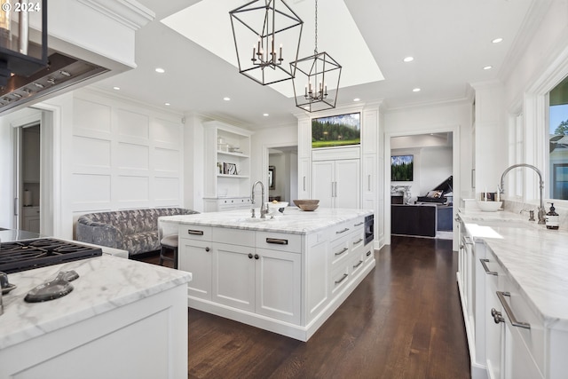 kitchen featuring crown molding, hanging light fixtures, an island with sink, light stone countertops, and white cabinets