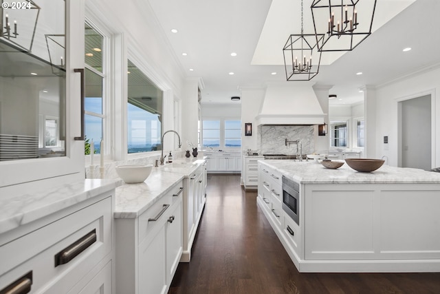 kitchen featuring pendant lighting, a center island with sink, custom exhaust hood, and white cabinets