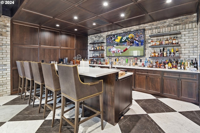 bar with coffered ceiling, dark brown cabinetry, and brick wall