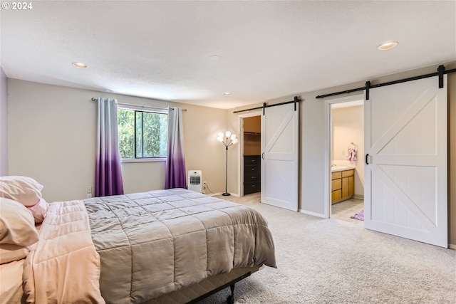 bedroom featuring a barn door, light colored carpet, and ensuite bath