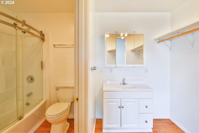 full bath featuring baseboards, toilet, wood finished floors, enclosed tub / shower combo, and vanity