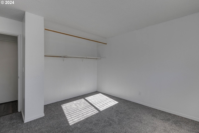 interior space featuring dark colored carpet, a textured ceiling, and a closet