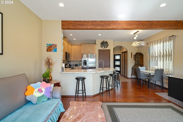 kitchen featuring a breakfast bar area, hanging light fixtures, beam ceiling, stainless steel appliances, and light brown cabinets