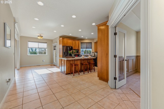 kitchen with a kitchen island, a kitchen breakfast bar, stainless steel fridge with ice dispenser, light stone counters, and light tile patterned floors