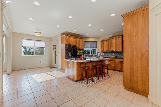 kitchen featuring stainless steel refrigerator with ice dispenser, a kitchen island, backsplash, light stone counters, and a breakfast bar area