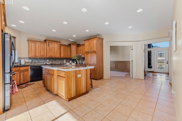 kitchen featuring light stone countertops, a kitchen island, black dishwasher, stainless steel fridge, and light tile patterned flooring