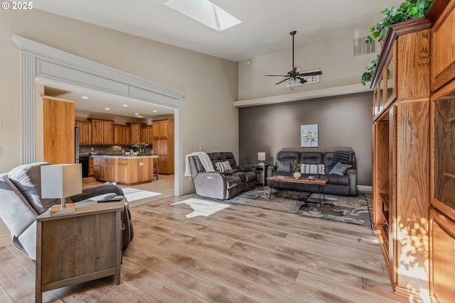 living room featuring light wood-type flooring, ceiling fan, and lofted ceiling with skylight