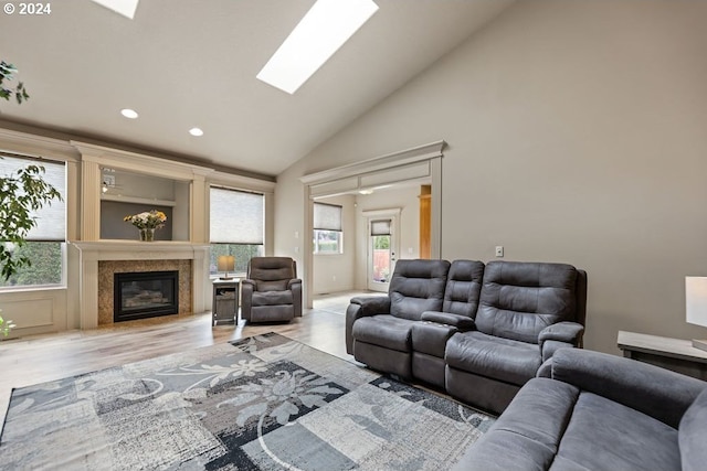 living room featuring light hardwood / wood-style floors, a high end fireplace, a skylight, and high vaulted ceiling