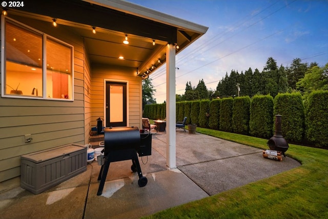 patio terrace at dusk with a yard and area for grilling