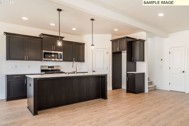 kitchen with sink, decorative light fixtures, stainless steel appliances, and a center island with sink