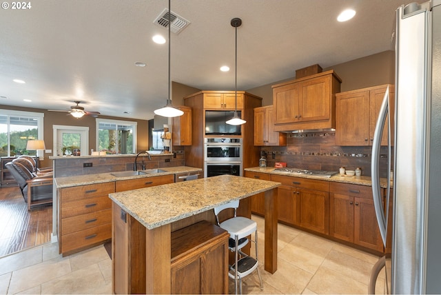 kitchen featuring pendant lighting, a kitchen island, stainless steel appliances, light stone countertops, and a kitchen bar