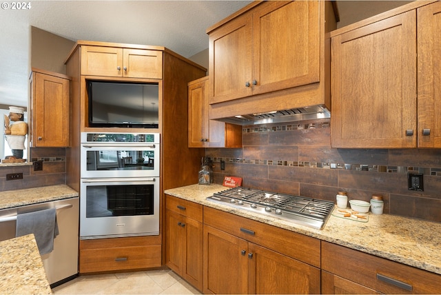 kitchen featuring light stone counters, stainless steel appliances, backsplash, and light tile patterned floors