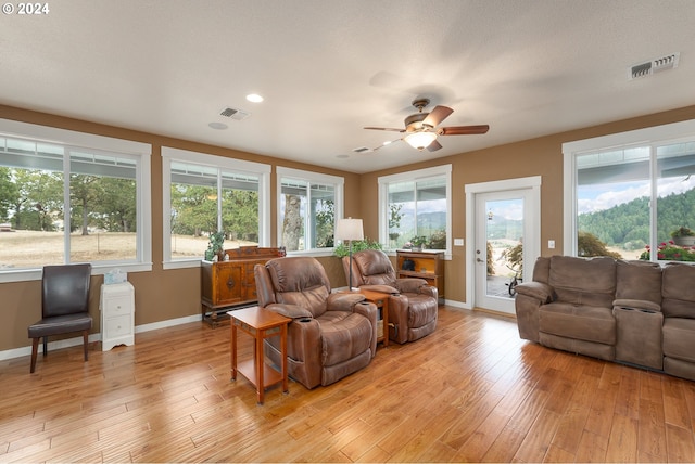 living room with ceiling fan, a textured ceiling, and light hardwood / wood-style flooring