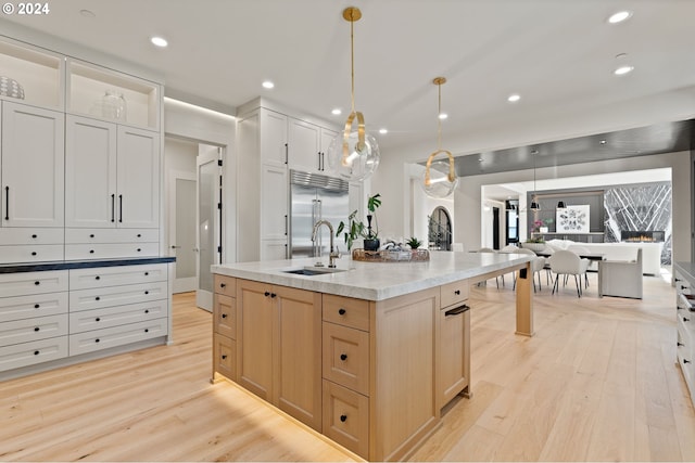 kitchen featuring stainless steel built in refrigerator, an island with sink, light hardwood / wood-style flooring, and sink