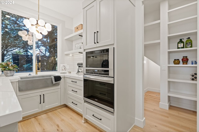 kitchen featuring white cabinets, light wood-type flooring, oven, decorative light fixtures, and sink