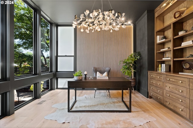 office with light wood-type flooring, a wall of windows, an inviting chandelier, and built in features