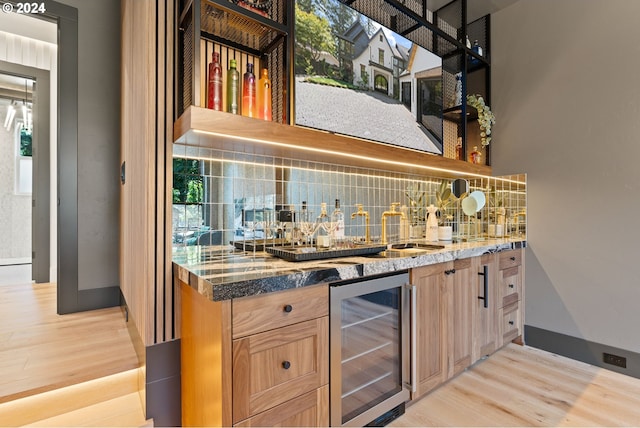 bar with light wood-type flooring, backsplash, dark stone countertops, and wine cooler