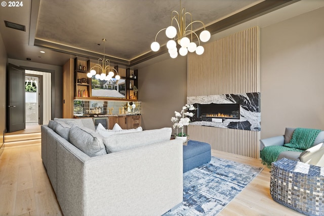 living room featuring light hardwood / wood-style flooring, a chandelier, a raised ceiling, and a fireplace