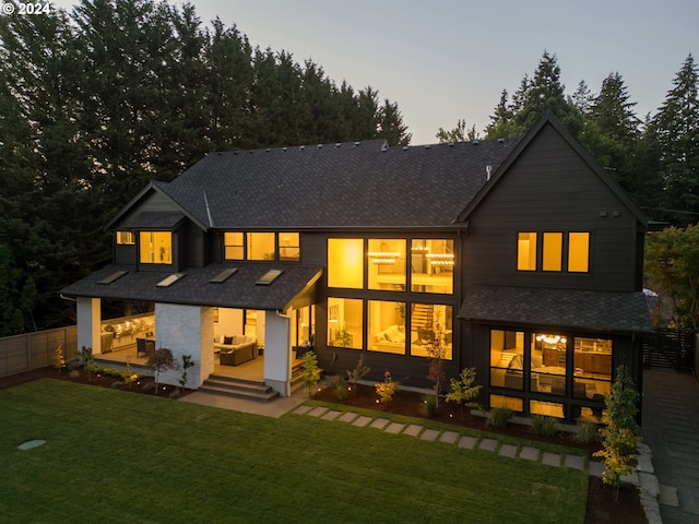 back house at dusk featuring a yard and a patio area