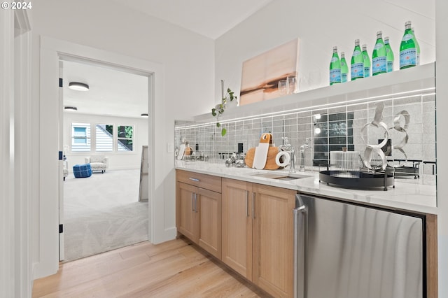 kitchen with light wood-type flooring, sink, stainless steel refrigerator, light stone countertops, and decorative backsplash