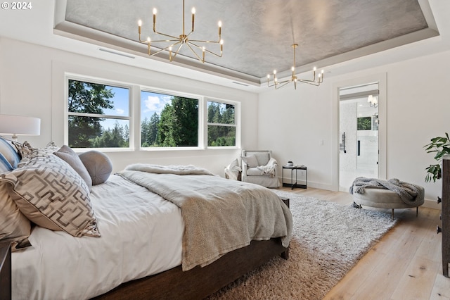 bedroom featuring light hardwood / wood-style flooring, a chandelier, and a raised ceiling