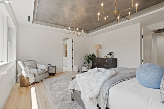 bedroom with a notable chandelier, a tray ceiling, ensuite bathroom, and hardwood / wood-style floors