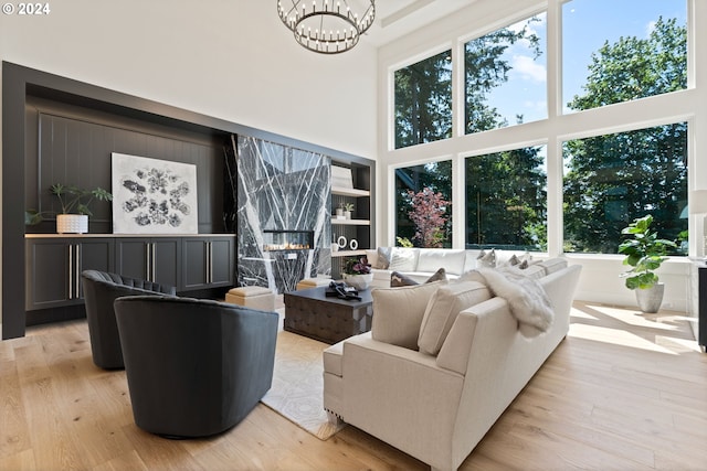 living room featuring light hardwood / wood-style floors, a high ceiling, a fireplace, and an inviting chandelier