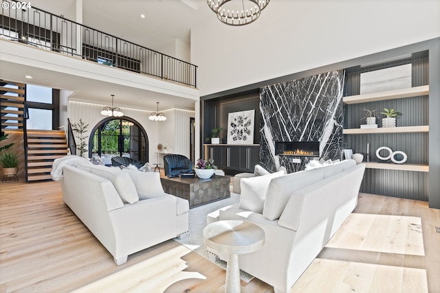 living room with an inviting chandelier, a towering ceiling, a high end fireplace, and light hardwood / wood-style floors