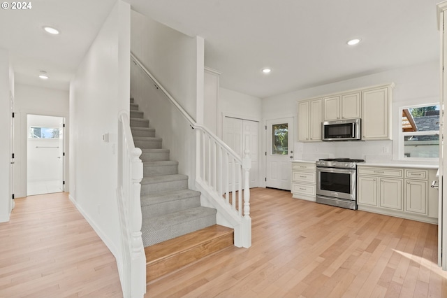 kitchen featuring a wealth of natural light, stainless steel appliances, cream cabinetry, and light hardwood / wood-style flooring