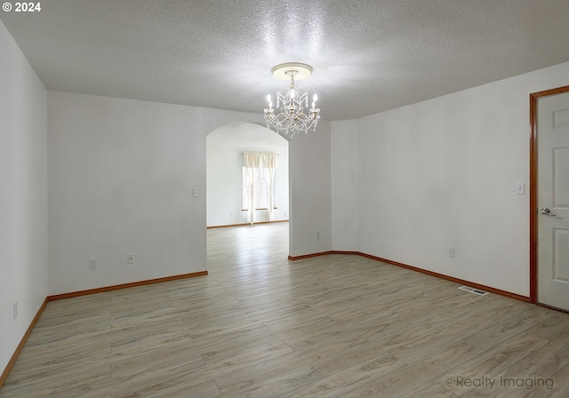 spare room featuring a textured ceiling, an inviting chandelier, and light hardwood / wood-style flooring