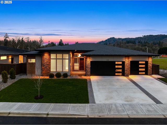 prairie-style house featuring a garage, stone siding, concrete driveway, and a yard