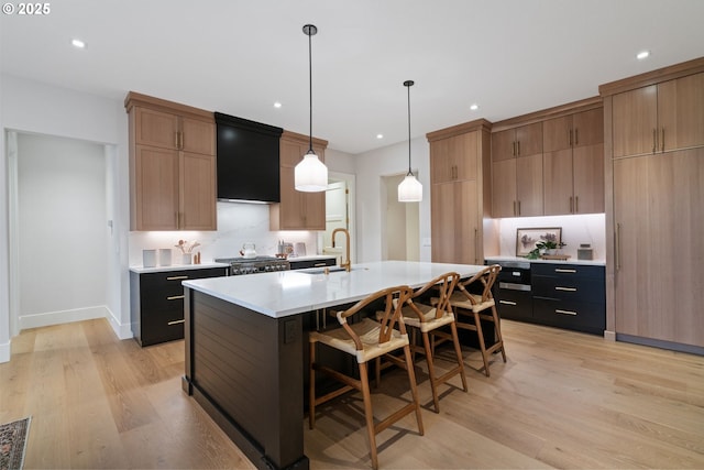 kitchen featuring light wood finished floors, decorative backsplash, an island with sink, light countertops, and a sink