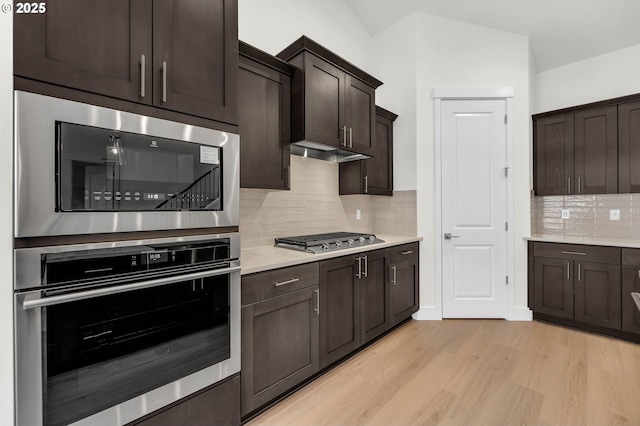 kitchen with tasteful backsplash, dark brown cabinets, light hardwood / wood-style flooring, and appliances with stainless steel finishes