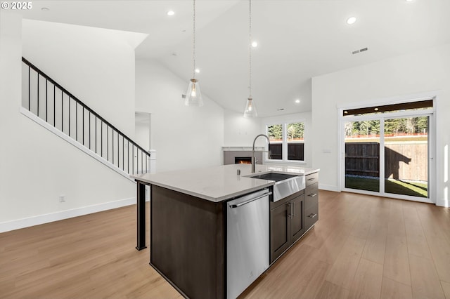 kitchen with a kitchen island with sink, sink, dishwasher, and light wood-type flooring