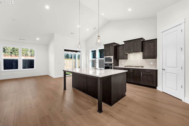 kitchen with appliances with stainless steel finishes, sink, a breakfast bar area, hanging light fixtures, and a kitchen island with sink