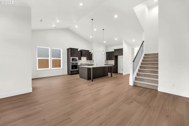 kitchen featuring hardwood / wood-style flooring, stainless steel microwave, high vaulted ceiling, and a center island with sink