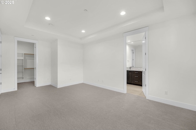 unfurnished bedroom with ensuite bathroom, a spacious closet, a raised ceiling, light carpet, and a closet