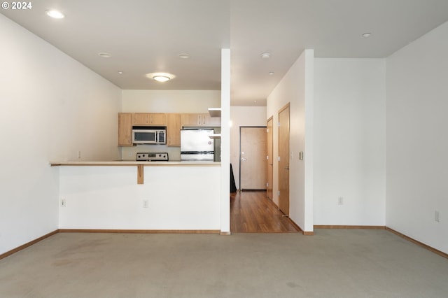 kitchen with kitchen peninsula, light brown cabinetry, and white appliances