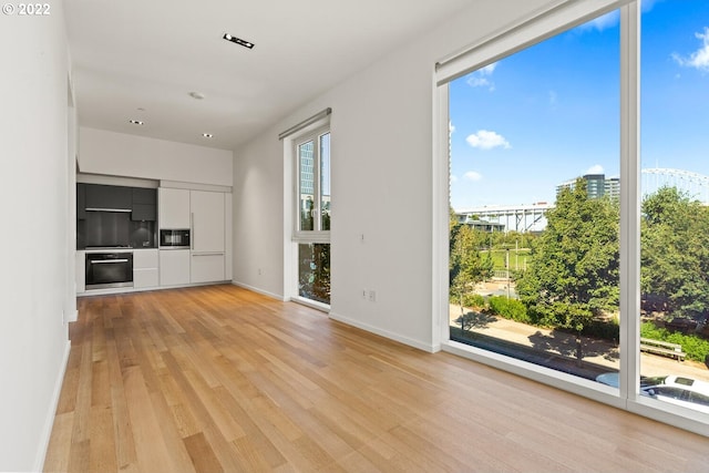 unfurnished living room featuring a view of city, light wood-type flooring, and baseboards