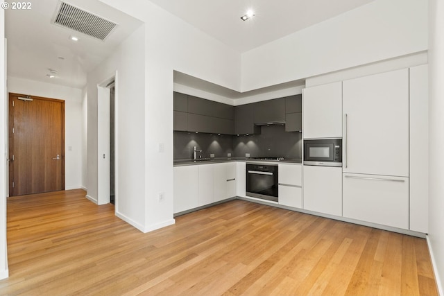 kitchen featuring wall oven, visible vents, light wood-type flooring, built in microwave, and modern cabinets