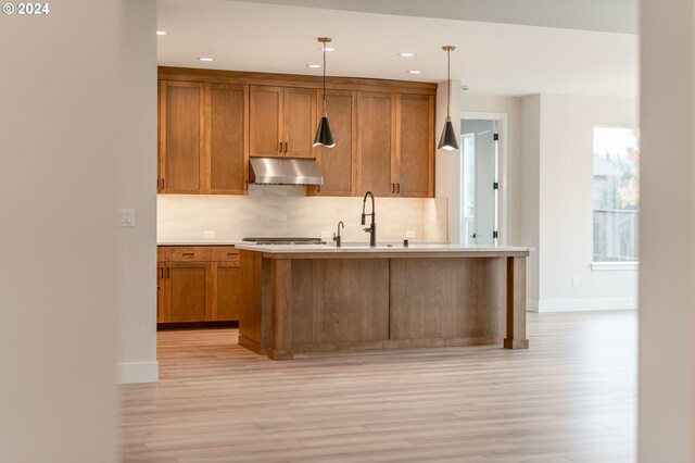 kitchen with a center island with sink, hanging light fixtures, tasteful backsplash, light hardwood / wood-style floors, and stainless steel appliances