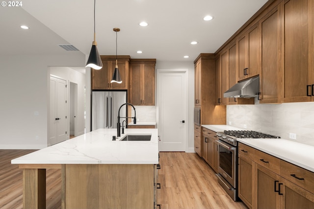 kitchen with high quality appliances, a center island with sink, sink, light hardwood / wood-style flooring, and decorative light fixtures