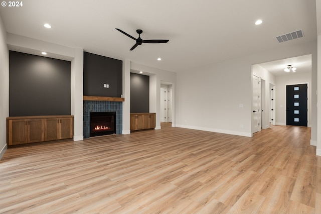 unfurnished living room featuring light hardwood / wood-style floors, ceiling fan, and a tiled fireplace