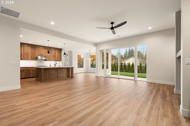 unfurnished living room with ceiling fan with notable chandelier and light hardwood / wood-style flooring