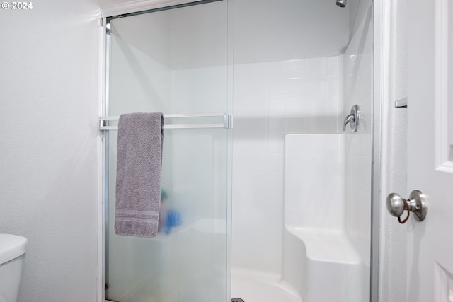 bathroom featuring a shower with door and toilet