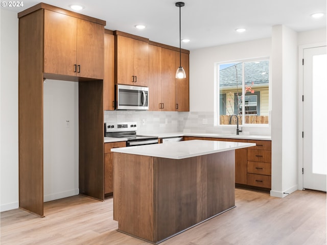 kitchen with sink, a kitchen island, pendant lighting, stainless steel appliances, and light hardwood / wood-style floors