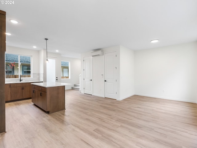 kitchen with hanging light fixtures, a kitchen island, an AC wall unit, and light hardwood / wood-style floors