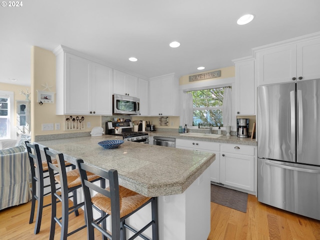 kitchen featuring white cabinets, appliances with stainless steel finishes, kitchen peninsula, a breakfast bar, and light hardwood / wood-style flooring